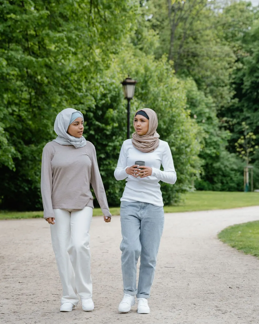 Two women walking and talking together along a path in a green park